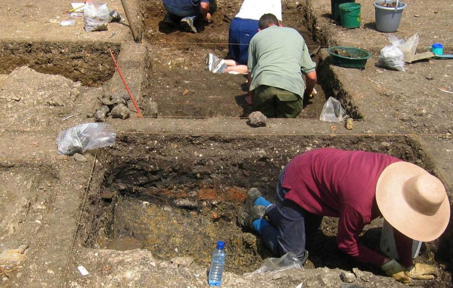 Four people digging in two trenches, surrounded by buckets, find bags, and water bottles.