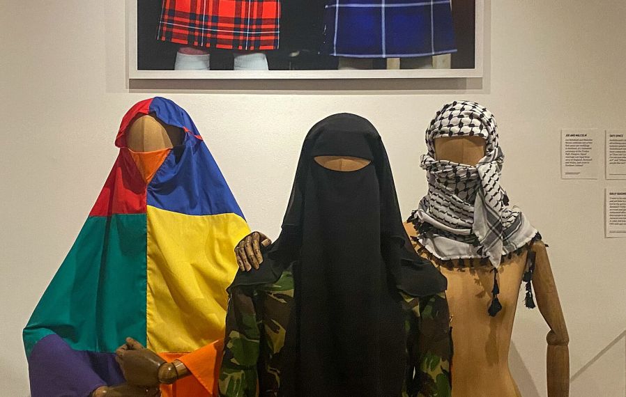 A rainbow khijmar is displayed alongside a camouflage shalwar kameez and a Palestinian Keffiyeh.