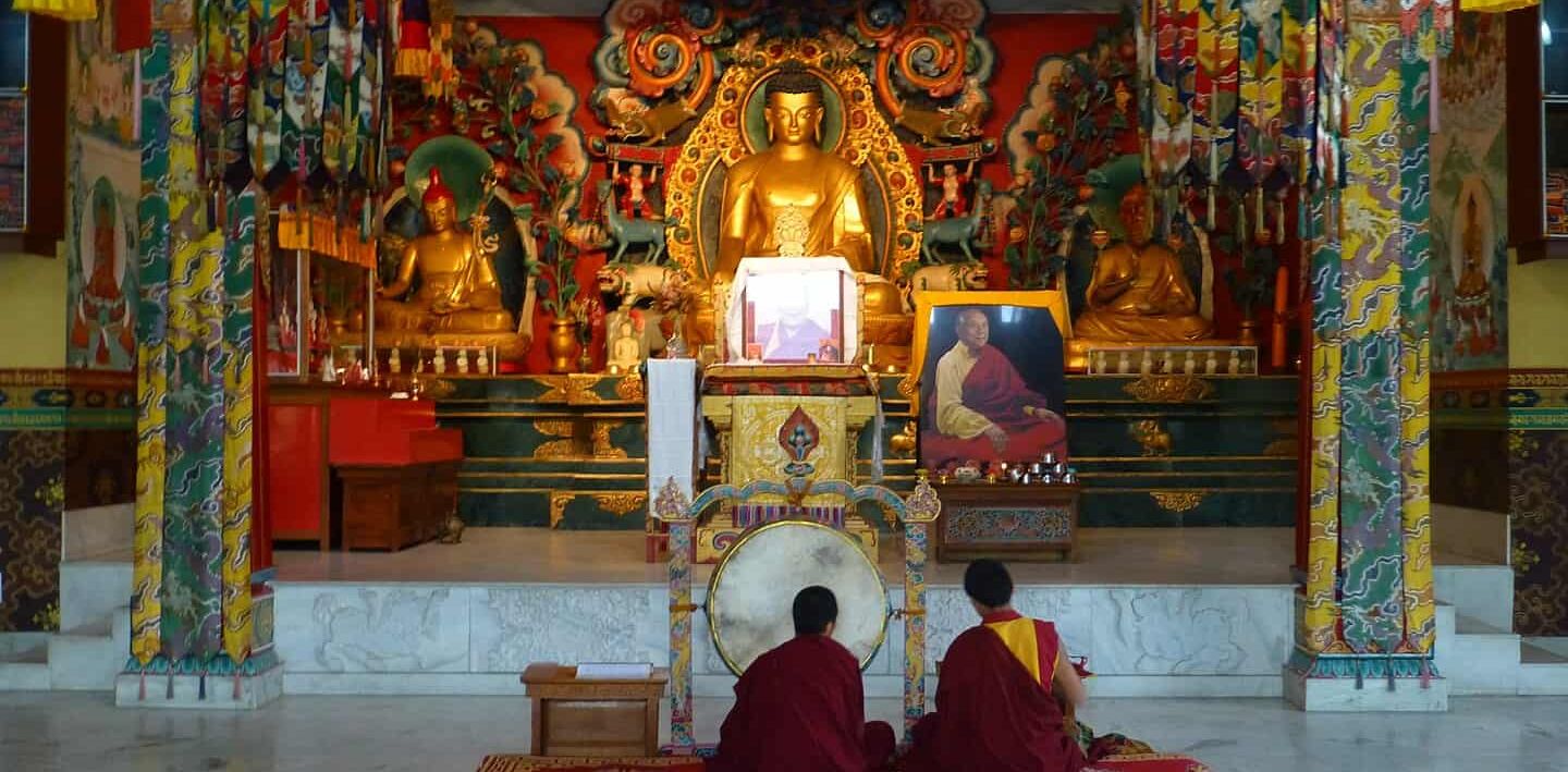 Inside a Tibetan Temple, Bodhgaya, with two people sat before a gold statue of Buddha.