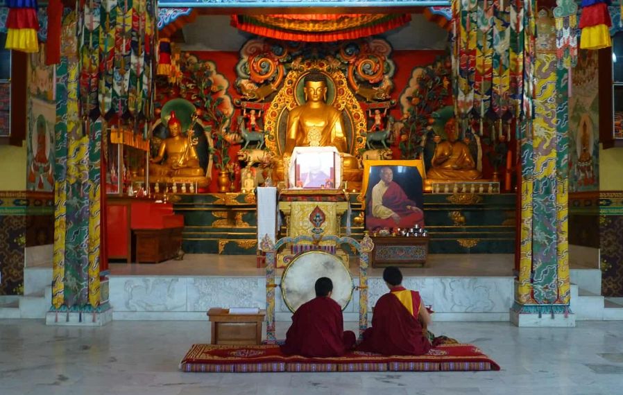 Inside a Tibetan Temple, Bodhgaya, with two people sat before a gold statue of Buddha.