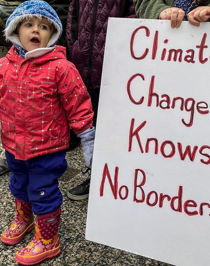 Child at a climate protest beside a sign reading 'Climate Change Knows No Borders'.