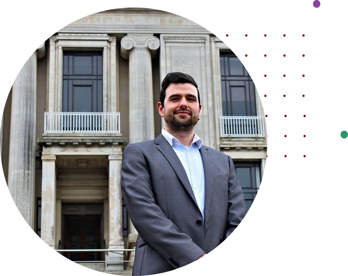 A man in a grey suit standing outside a grand stone building with columns
